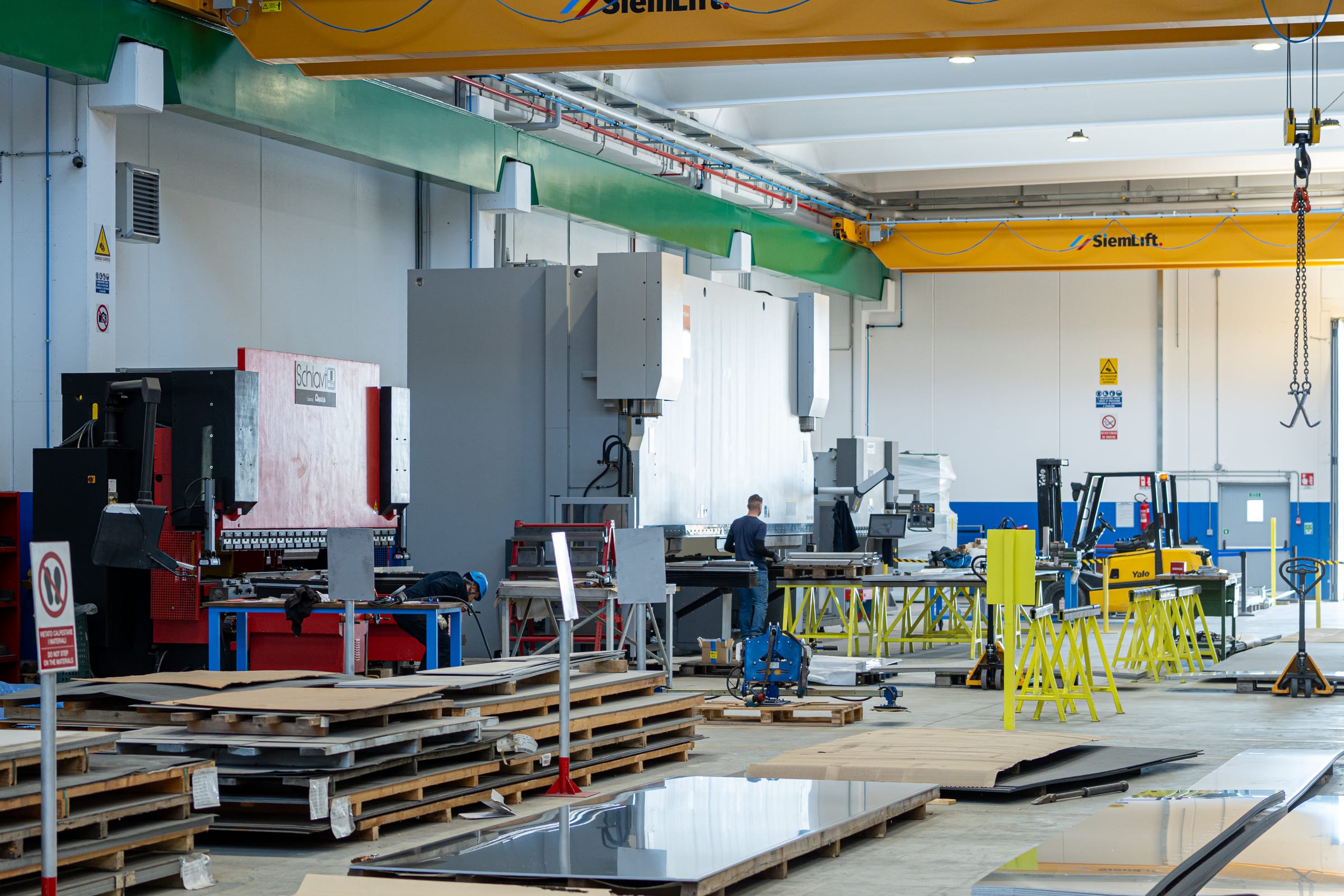 Overview of the Albizzati workshop in Magenta with overhead cranes, press brake and steel sheets on the floor