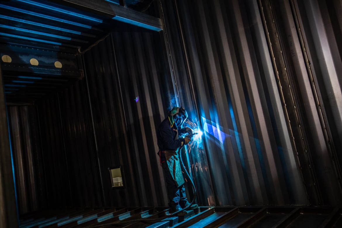 Welder at work inside the corrugated steel shell of a prefabricated module