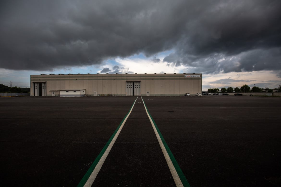 Wide yard with painted lane leading to the production hall under dark clouds